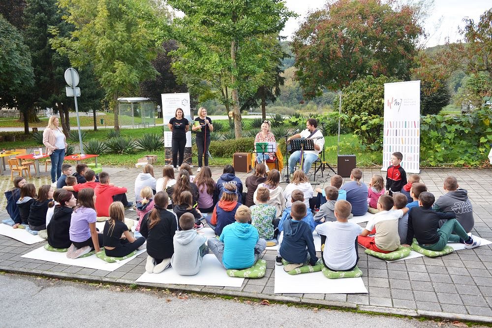 koncert Anje Pavlin, otroci sedijo na tleh in poslušajo glasbo